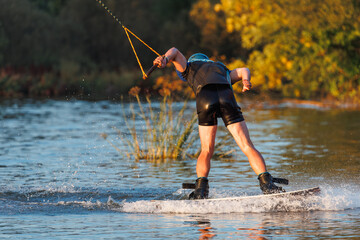 An athlete performs a trick on the water. Park at sunset. Wakeboard rider