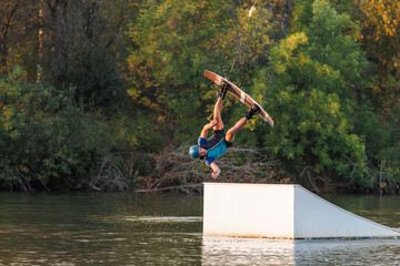An athlete jumps from a springboard. Wakeboard park at sunset. A man performs a trick on a board