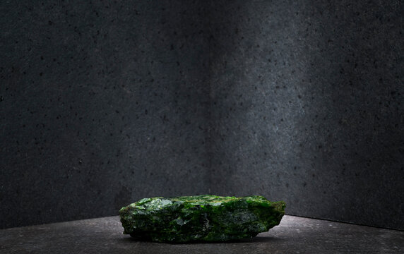 green chrome diopside stone on a dark gray background for a product presentation podium. natural green stones on a gray background for the presentation of perfumes, jewelry, cosmetics, medicines.