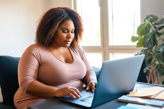 Full figured overweight African American woman working from home on a laptop computer