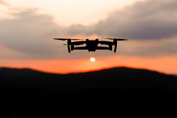 Fototapeta na wymiar The silhouette of a drone flying over the mountains line at sunset.