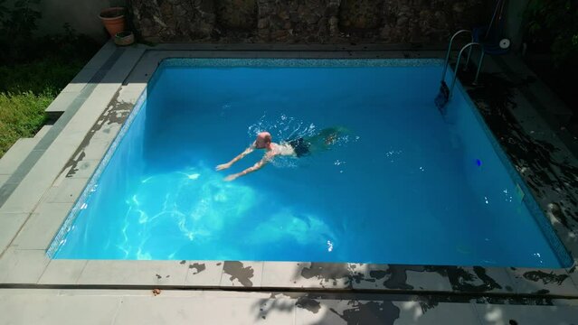 Top view of a hotel pool on a hot summer sunny day, one short-haired man swims from the pool riser to one of the sides, then swims from side to side