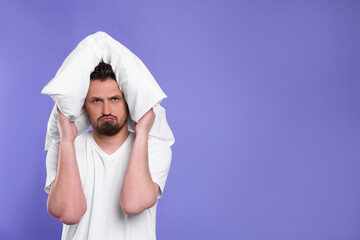 Unhappy man covering ears with pillow on violet background, space for text. Insomnia problem