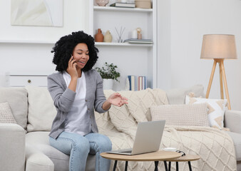 Happy young woman talking on phone while using laptop at coffee table indoors. Space for text