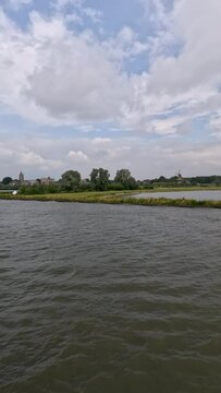 Approaching the river port in Gorinchem, Netherlands along the Rhine River. Views from a river boat sailing to shore. A traditional Dutch windmill (Dalempoort) can be seen 
