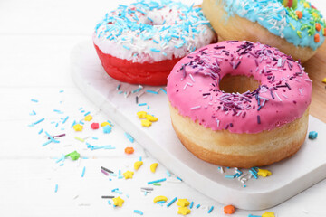 Sweet glazed donuts decorated with sprinkles on white wooden table, space for text. Tasty confectionery