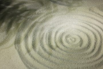 Fototapeta na wymiar Beautiful spiral and shadows of leaves on sand, closeup. Zen garden