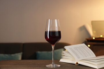 Glass of red wine and open book on wooden table in room. Relax at home