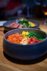 Poke bowl with salmon, rice, avocado, edamame beans, cucumber and radish in a gray bowl. Hawaiian ahi poke bowl, gray background