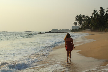 Woman wearing a red dress walking at the ocean beach in Unawatuna, Sri Lanka