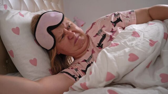 Woman in pajamas, mask goes to bed sleep, turns around, tosses and turns, unpleasant smell interferes, farting, children scattered toy Parenting, funny family pranks. Cozy bed, uncomfortable mattress