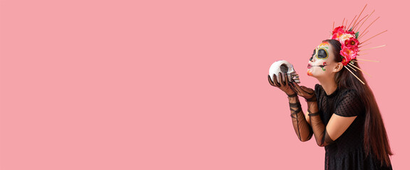 Young woman with painted skull on pink background with space for text. Mexico's Day of the Dead (El Dia de Muertos)