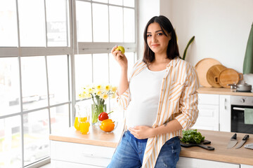 Young pregnant woman with apple in kitchen