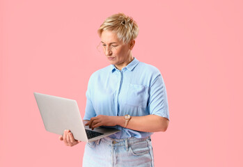Mature female programmer working with laptop on pink background