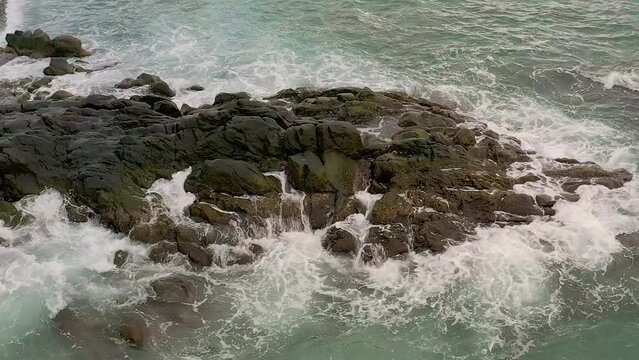 Cinematic aerial slow motion shot of waves washing over the rocky coastline of Looc Beach in Surigao City, Philippines.