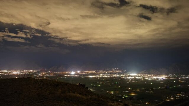 Timelapse of cars driving at night through Utah Valley as lightning flashes as storm moves over the mountains at night.
