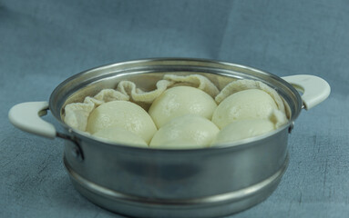 The image is of a bean paste bun sitting in a steamer basket. Bean paste buns that look like steamed buns on the outside but are filled with red bean paste on the inside. 