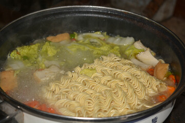 Photo of a pot of noodles being cooked with some vegetable toppings