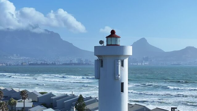 Cape Town and Table Mountain in background of a lighthouse on the shore of Table Bay. Zoomed-in drone footage, slow camera movement across to reveal the famous mountain behind. 