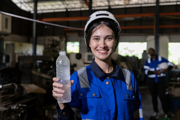 Women engineer smiling holding water drink from plastic bottle at factory during break. Drinking...