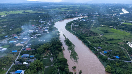 Fototapeta premium Aerial view of the Ping River across rice fields and rural villages during sunset. Views of Chiang Mai villages and the Ping River from a drone.