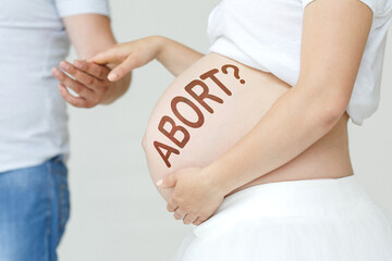 A pregnant woman holds her husband's hand on her stomach with the inscription - ABORTION, a...