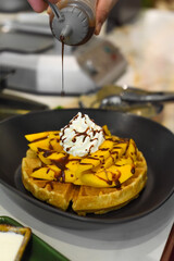 the cook putting chocolate syrup on fresh sliced mango fruit on baked belgian waffles