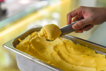 hand scooping a scoop of Passion fruit ice cream into a spoon in fridge