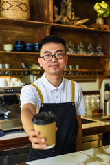 Fototapeta na wymiar Vietnamese smiling waiter holding paper cups with coffee in a cafe