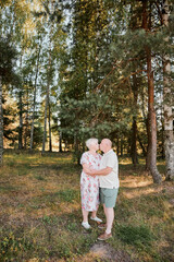Naklejka na ściany i meble An elderly couple in love walks in the park and hugs each other. Love through the years