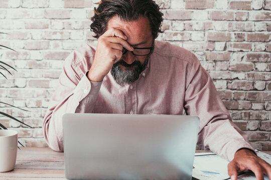 Portrait of man working on laptop with problems. Connections or security. Modern male adult people lifestyle. Professional freelance touching his front worries in front of a computer on the desk home