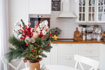 A spruce bouquet with red berries, toys, cotton on a white kitchen table. Christmas decorations in the interior. The concept of preparation for the New Year's holiday 2024.