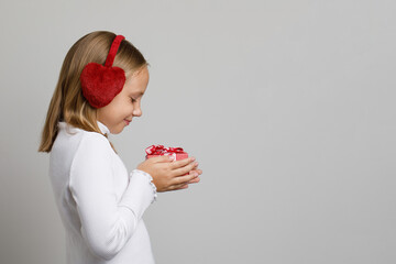 Portrait of cute smiling child girl in earmuffs with red surprise gift present on white background