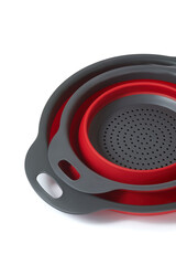 Close-up shot of two different sized foldable silicone colanders with handles. Set of two colanders with red inserts is isolated on a white background. Top view.