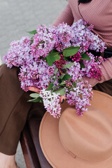 A bouquet of lilacs in the hands of a girl and a hat