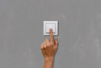 Female finger on light switch close-up on grey concrete wall background.