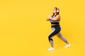 Fototapeta na wymiar Full body side view young plus size big fat fit woman wear blue top warm up training listen to music in headphones do squates isolated on plain yellow background studio home gym Workout sport concept