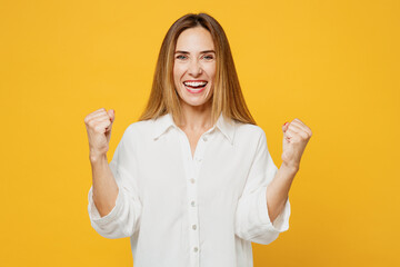 Young overjoyed caucasian happy woman she wears white shirt casual clothes doing winner gesture celebrate clenching fists say yes isolated on plain yellow background studio portrait Lifestyle concept