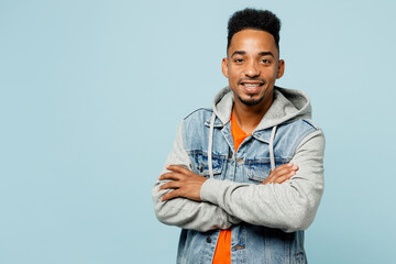 Young smiling happy man of African American ethnicity wear denim jacket orange t-shirt hold hands crossed folded look camera isolated on plain pastel light blue background studio. Lifestyle concept.