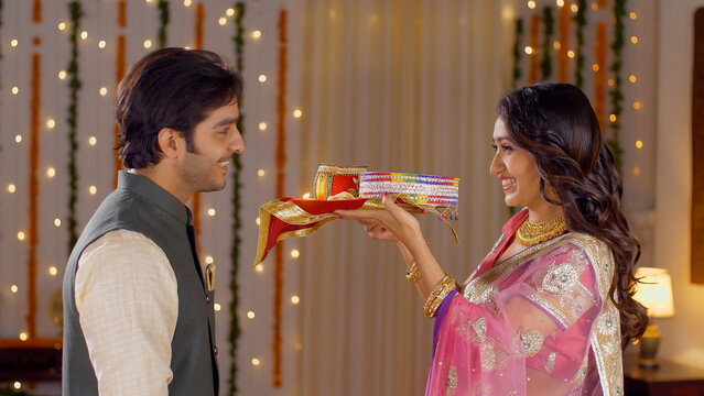 Newly married couple celebrating their first Karwa Chauth together - Indian festival. Young beautiful wife performing Karwa Chauth traditions with her husband  praying for his long and safe life in...