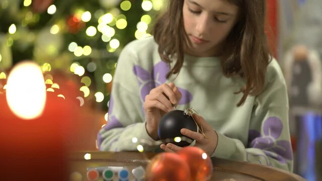 A girl painting Christmas decorations on Christmas eve, prepares for the celebration and decorates the Christmas tree