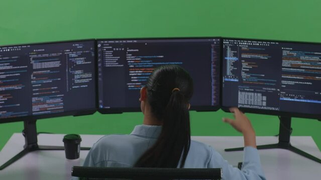 Back View Of Asian Woman Developer Having Headache While Write Code With Multiple Computer Screens In Green Screen Studio
