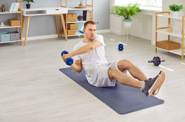 Sporty, motivated, young man doing active physical exercises on a rubber mat with dumbbells during...