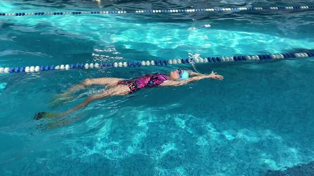 4K A beautiful ten-year-old girl learns to swim. Children practice with fins for swimming in the pool.