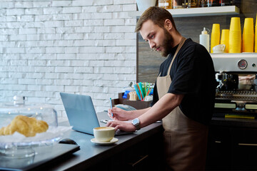 Owner coffee shop worker young male with laptop on the counter
