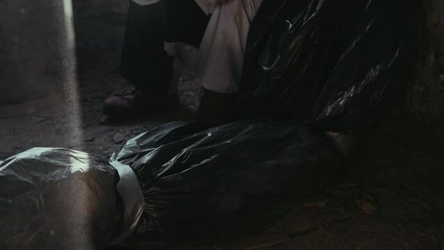 Tilt up shot of psycho clown hitting dead body in trash bag on floor of abandoned building