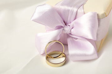 Gift box and wedding rings on white background, close up