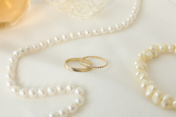 Wedding rings and pearl jewelry on white background, close up