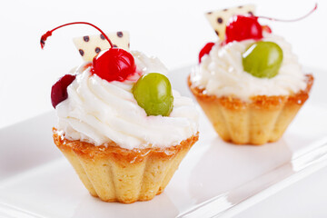Beautiful cream cakes with cherries and grapes on a plate on a white background