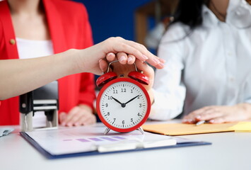 Two business women turning off alarm clock at workplace closeup. Terms of conclusion of contracts concept